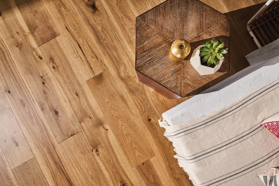 Wood floor with natural grain, an octagonal side table holding a small gold vase and a potted succulent, next to a beige blanket with black stripes and red accent pillow.