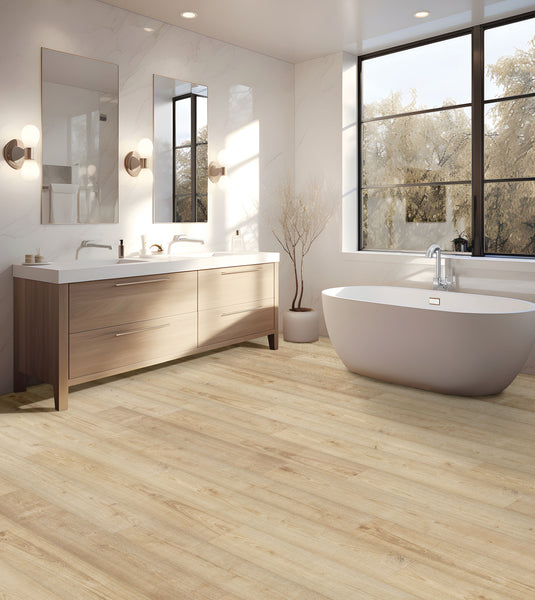 A modern bathroom with light wood floors, a freestanding white bathtub, double vanity with two mirrors, wall sconces, and large windows letting in natural light.