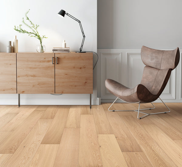 A modern, minimalist living space with light wood flooring, a tan and brown upholstered lounge chair, a wooden sideboard with decor items, a black desk lamp, and a white wainscoted wall.