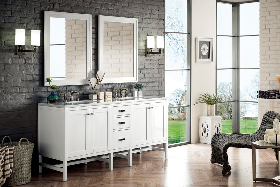 Bright, modern bathroom with double sinks, two large mirrors, wall lights, white cabinetry, gray brick accent wall, large windows with a garden view, and minimal decorative items.