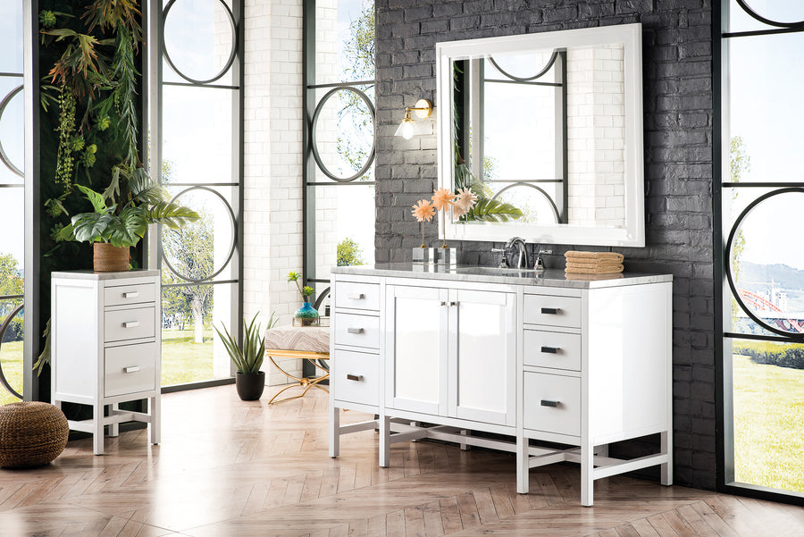 A modern bathroom with large circle-paned windows, a white vanity with drawers, a matching side cabinet, a large mirror, plants, and light wood herringbone floors. Natural light fills the space.