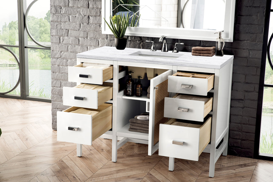 A modern white bathroom vanity with six open drawers, two open cabinet doors revealing shelves with towels and bottles, a potted plant, and a sink with a silver faucet beneath a large mirror.