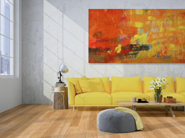 A modern living room with a yellow sofa, colorful abstract painting on the wall, wooden floor, side table with lamp and books, a glass vase of white flowers, and a round gray pouf. Sunlight streams in from large windows.