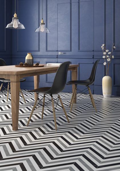A modern dining room with a wooden table, black chairs, Casablanca 8x8 Glazed Ceramic Patterned Tile floor in black and white, navy paneled walls, pendant lights overhead, and a tall vase with branches in the corner.