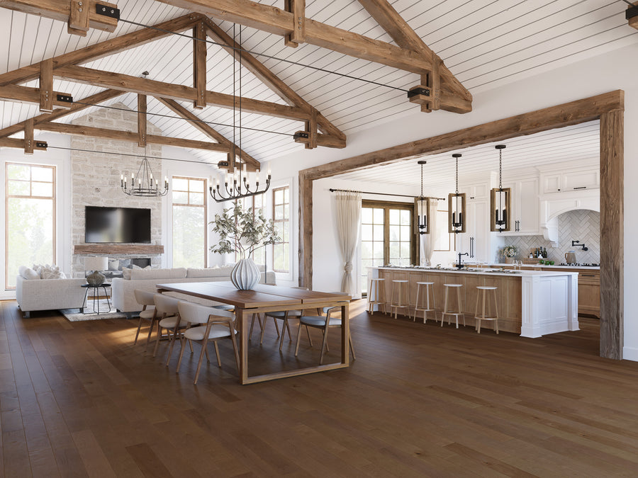 Spacious open-concept living area with exposed wooden beams, a modern kitchen with a large island and pendant lights, a dining table with chairs, and a cozy living room with sofas and a fireplace. Large windows let in natural light.