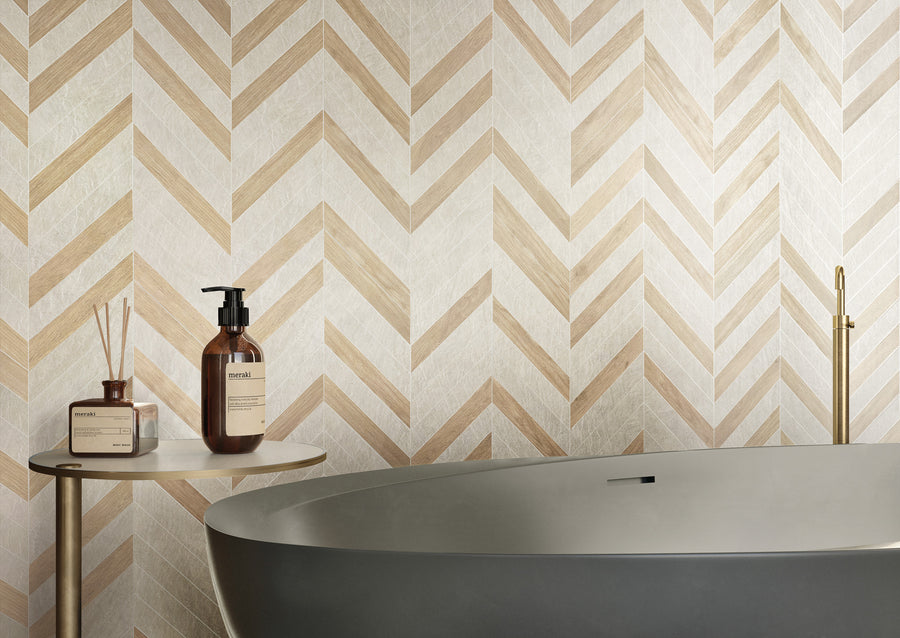 Modern bathroom with a matte gray freestanding tub, a round side table holding a soap dispenser and diffuser, and a beige and white chevron-patterned wall in the background.