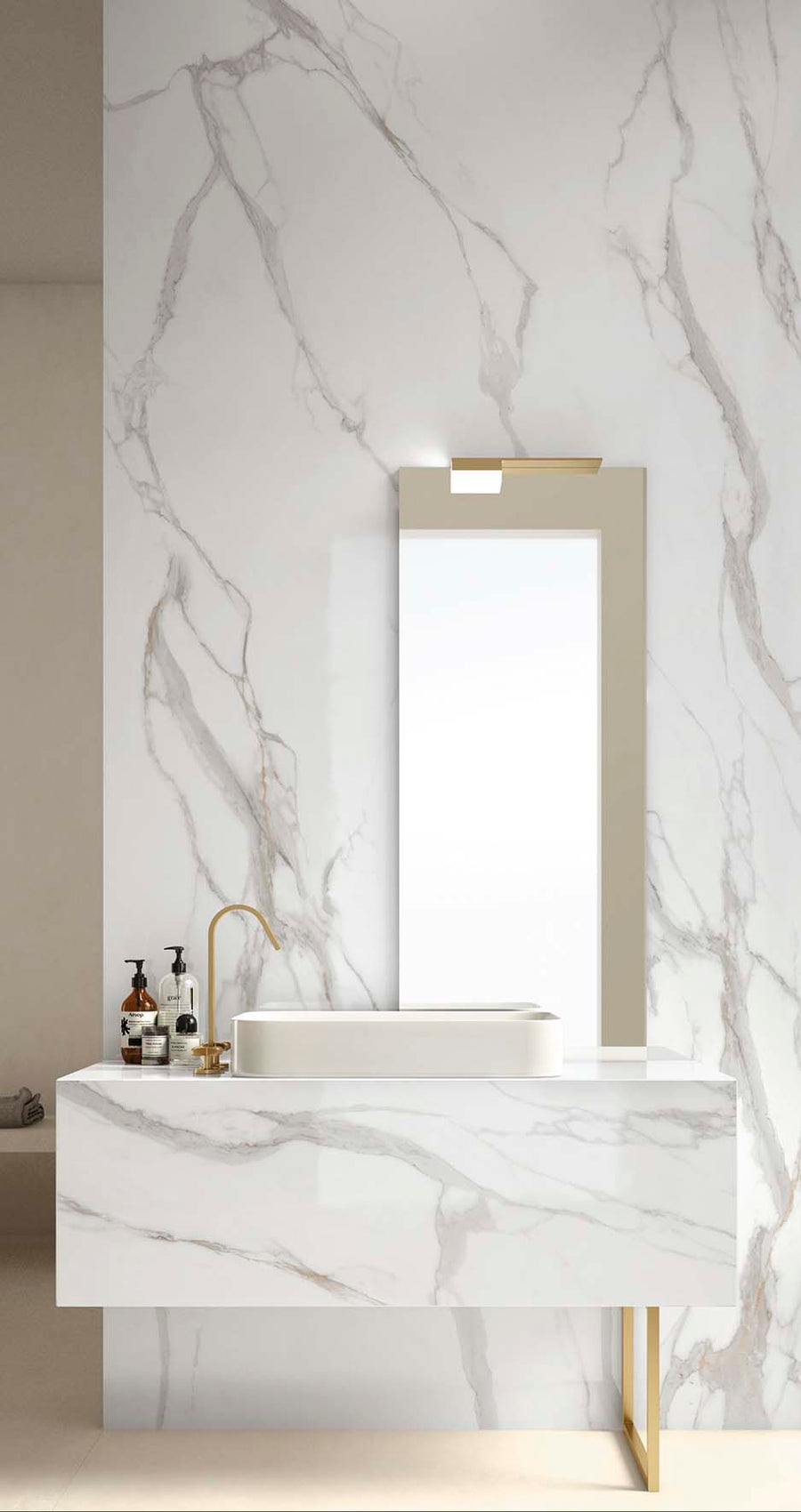 Modern bathroom with white marble walls and vanity, gold faucet, rectangular mirror with light, and toiletries on the counter. The design is minimalist and elegant.