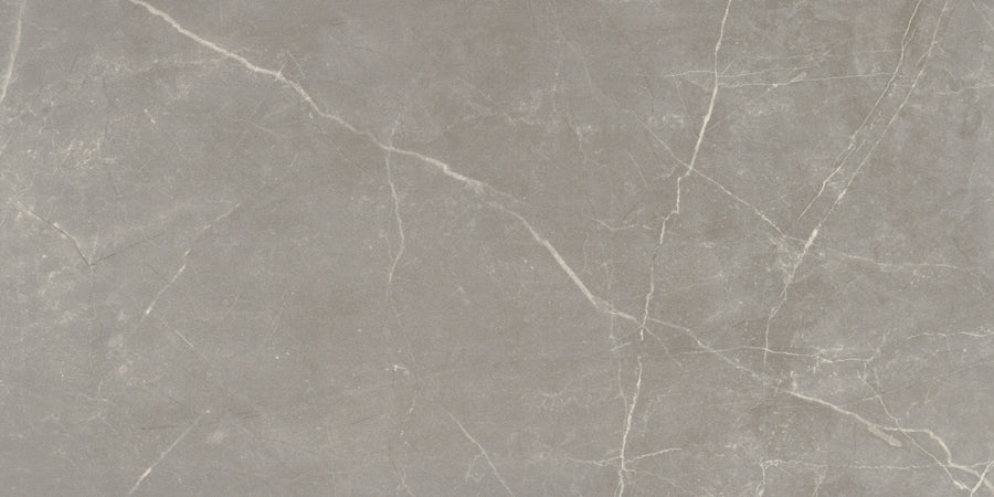 The Callie 12x24 Polished Porcelain Tile in Fog features a light gray surface with subtle white veining and natural-looking cracks, offering a textured, organic look that’s perfect for elegant interior spaces.