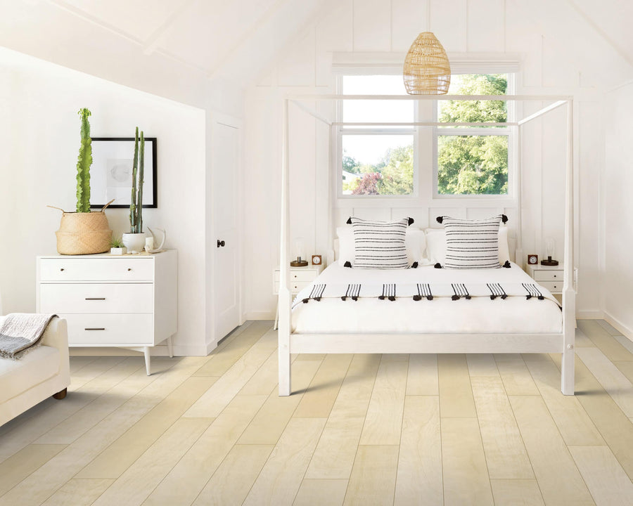 Bright, modern bedroom with a white canopy bed, striped pillows, a dresser with a tall potted cactus, a woven pendant light, and large windows letting in natural light. Pale wood floors complement the minimalist decor.