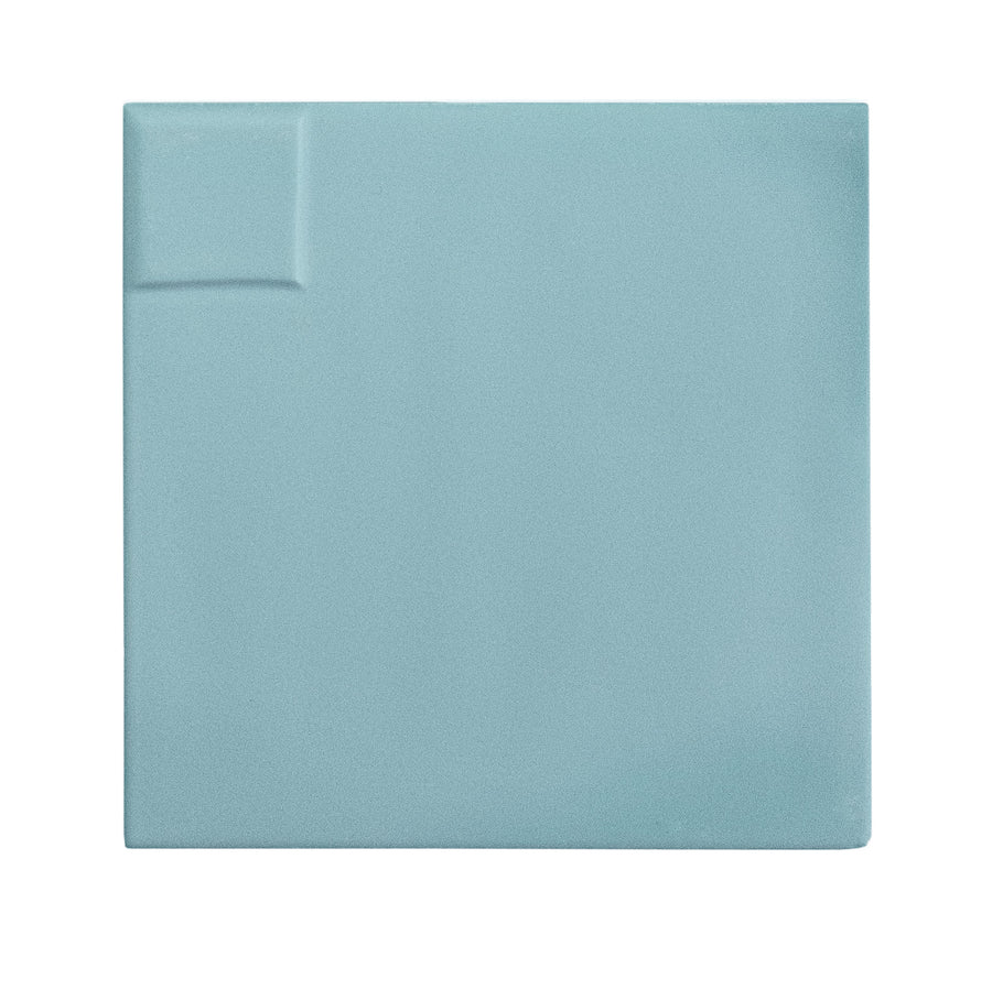 The Casbah Décor Mix 5" x 5" Ceramic Tile in Sky features a square, pale blue design with a small raised rectangular detail in the upper left corner, set against a white background.
