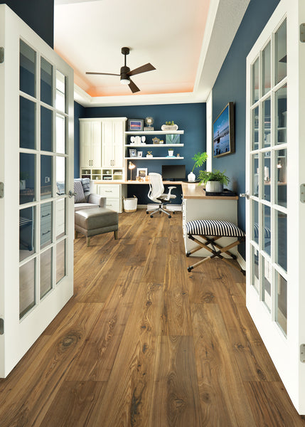 A modern home office with blue walls, wood flooring, French doors, built-in shelves, a desk with a computer, a white office chair, and a striped ottoman, with plenty of natural light.