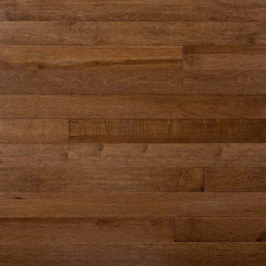 Close-up view of Champlain Maple ¾" x 3 1/4" Hardwood floorboards, featuring a natural brown finish with subtle wood grain patterns and gentle color variations across the dent-resistant planks.