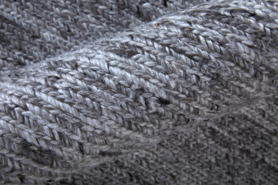Close-up of a soft, gray knitted fabric with a visible textured pattern. The yarn appears thick and the knitting style creates a cozy, warm appearance with a mix of light and dark gray tones.