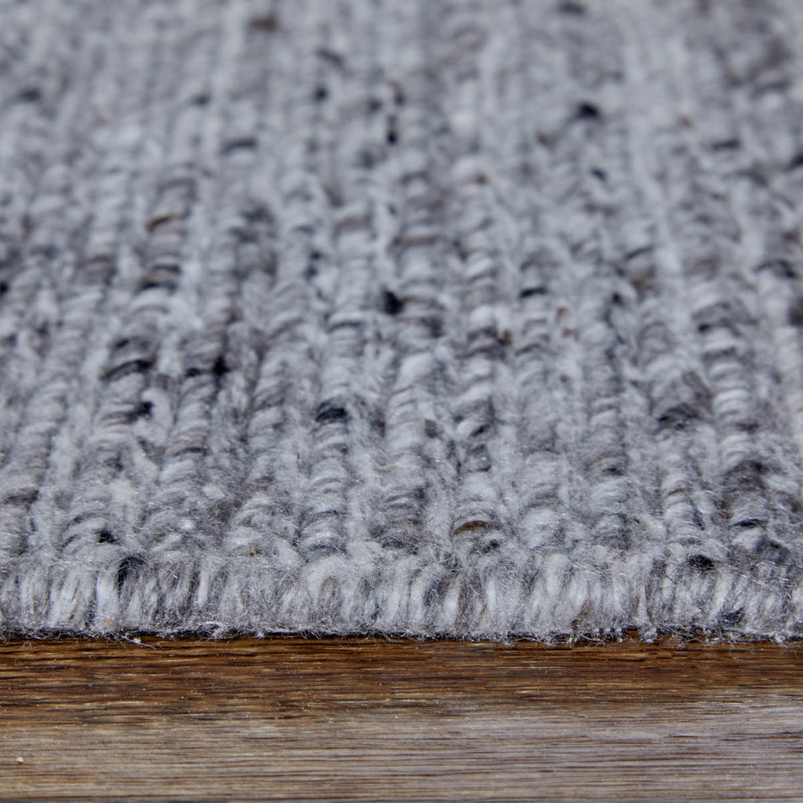 Close-up of a gray, textured, knitted rug or carpet with visible yarn patterns, placed on a wooden floor.