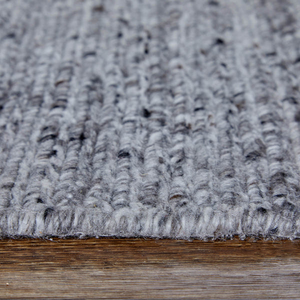 Close-up of a gray, textured, knitted rug or carpet with visible yarn patterns, placed on a wooden floor.