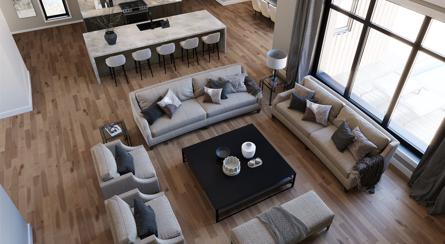 A modern living room with wood floors, neutral-toned sofas, a large black coffee table, and an open kitchen with a marble island and barstools. Large windows let in natural light, and décor includes throw pillows and candles.