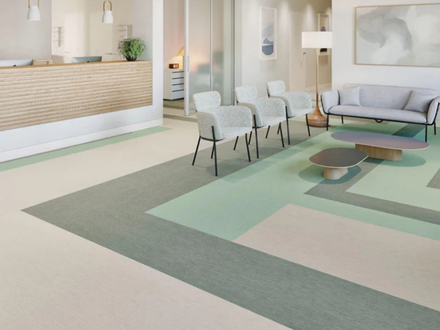 A modern reception area with a wooden front desk, light chairs, gray sofa, low tables, and abstract wall art. The floor features Commercial Vinyl in geometric patterns of muted green and beige.