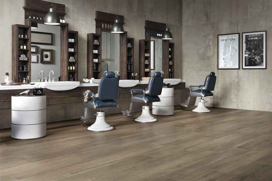 A modern barbershop with three vintage-style barber chairs, large mirrors, sinks, and shelves with grooming products along a concrete wall, and wooden flooring throughout the space.