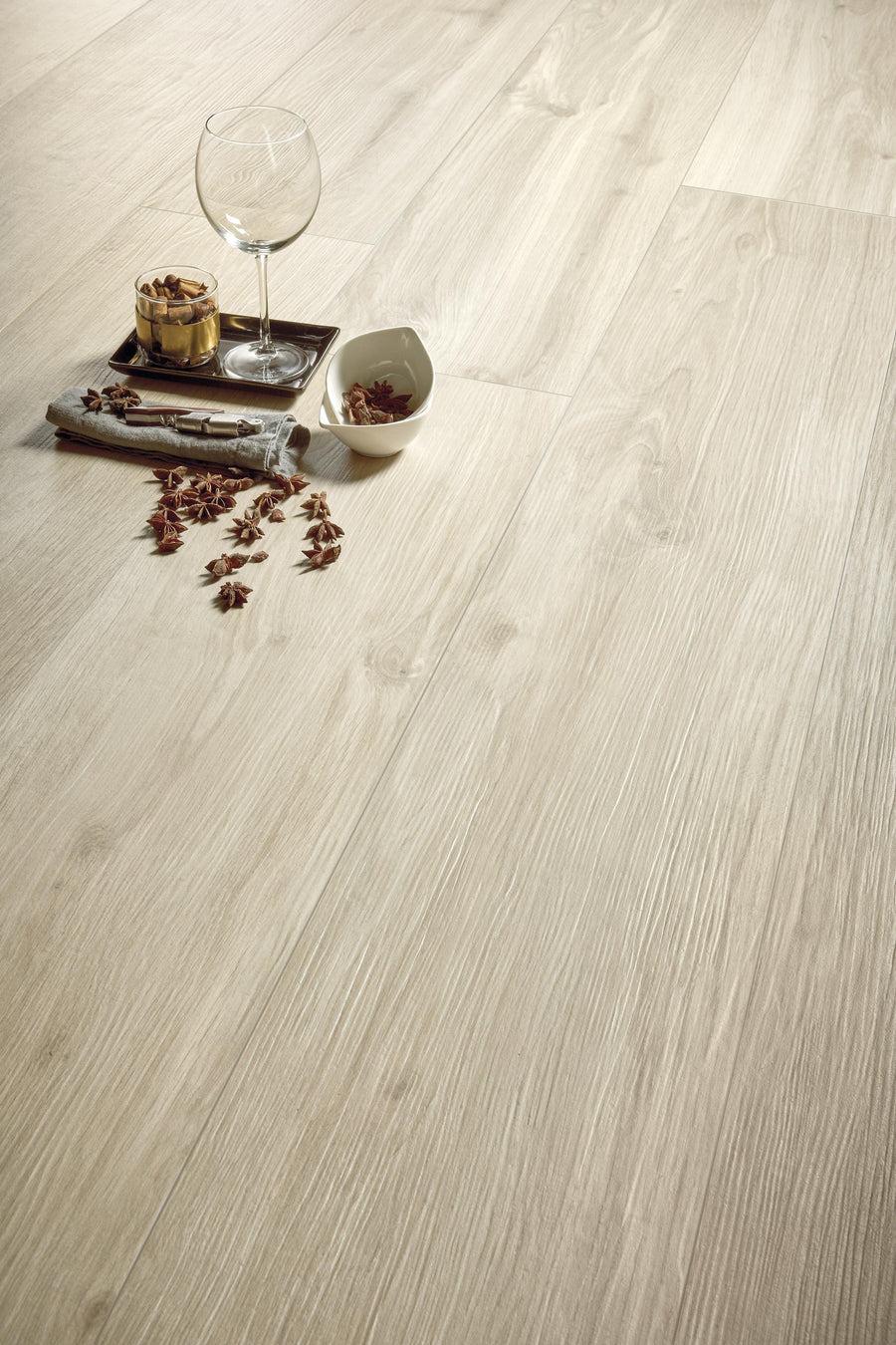 A close-up of light wood flooring with a tray holding a wine glass, a small bowl, a rolled-up napkin, and scattered star anise, creating an elegant and cozy atmosphere.