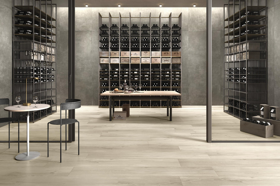 Modern wine cellar with tall shelves filled with wine bottles, a large wooden table in the center, and two small round tables with chairs in the foreground. The space has a sleek, minimalist design.