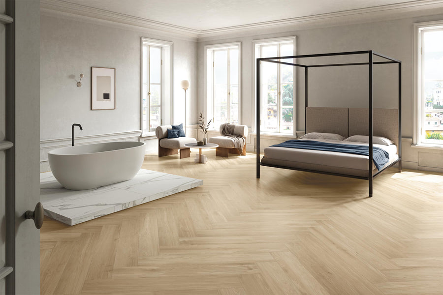 Spacious, modern bedroom with light wood herringbone floors, a black canopy bed, a freestanding white bathtub on a marble platform, large windows, and minimalistic furniture in neutral tones.