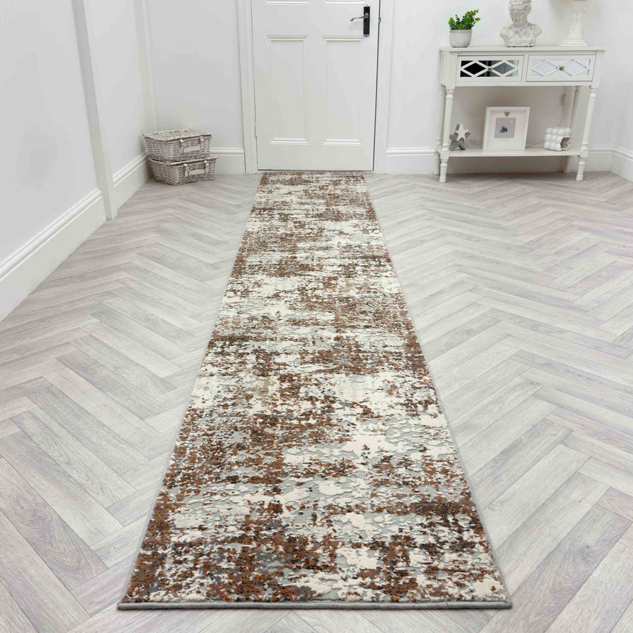 The Couture 52016-1626 Runner Rug in brown and gray patterns lies on a light herringbone wood floor, paired with a white console table and basket near the white door for a luxurious hallway look.