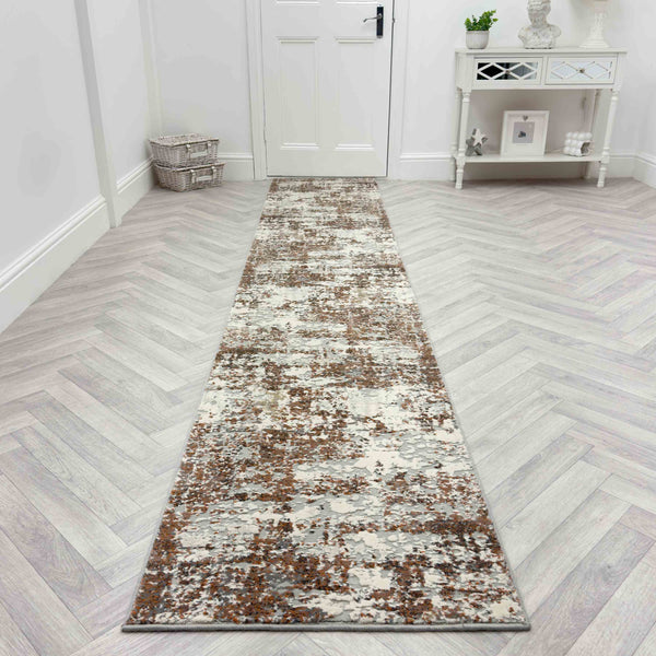 The Couture 52016-1626 Runner Rug in brown and gray patterns lies on a light herringbone wood floor, paired with a white console table and basket near the white door for a luxurious hallway look.