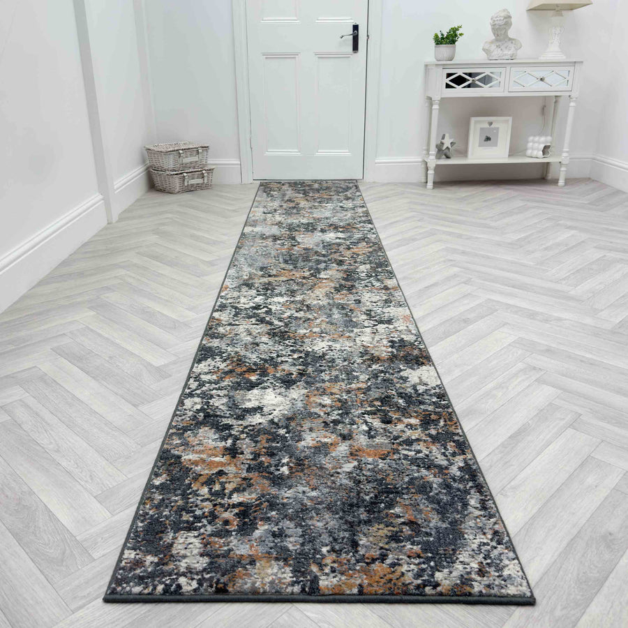 The Couture 52023-6616 Runner Rug, featuring a marbled pattern in gray, black, and brown tones, adds a touch of luxury on a light herringbone floor in a bright hallway with white walls and furniture.