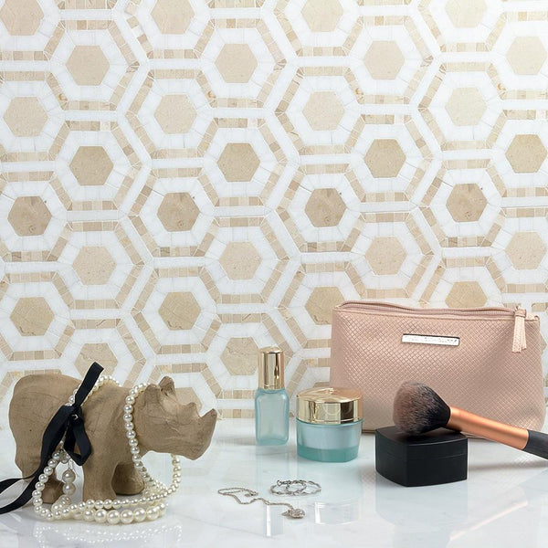 A vanity setup with a pink makeup bag, two blue cosmetic jars, a makeup brush, jewelry including a pearl necklace and earrings, and a decorative rhino head, all set against a beige geometric tile wall.