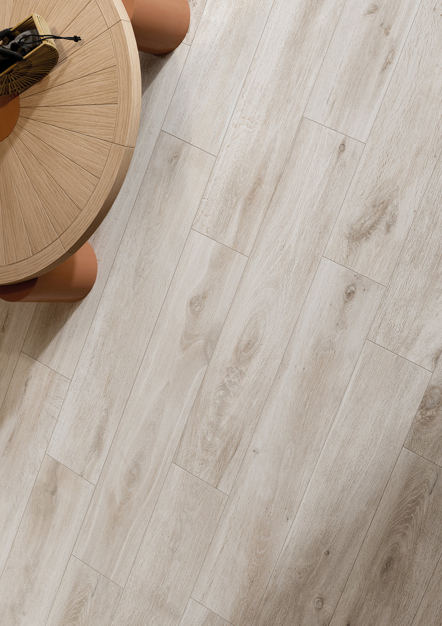 A round wooden table with a light natural finish is partially visible on the left, placed on a floor with light wood-look planks featuring subtle grain patterns.