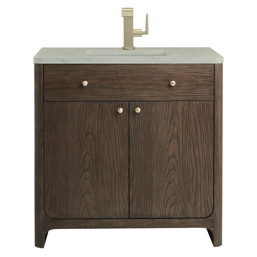 A bathroom vanity with a white marble countertop, brass faucet, two small brass knob handles on upper drawer, and two brass knobs on double wooden cabinet doors with a dark wood grain finish.