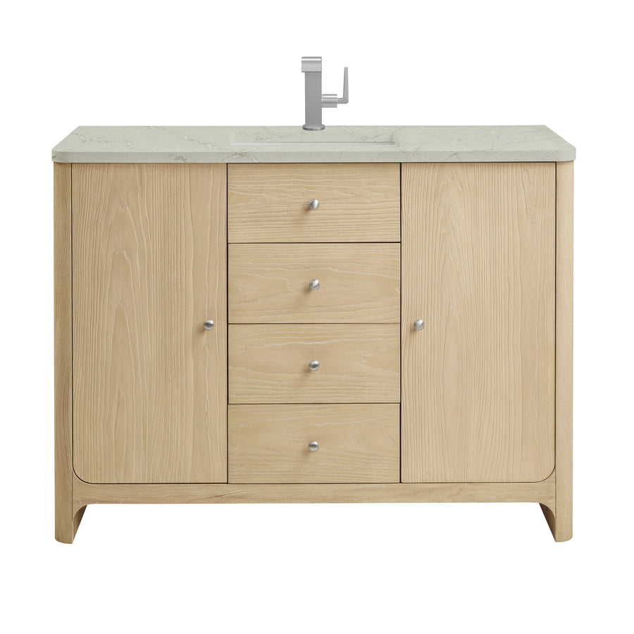 A light wood bathroom vanity with a marble countertop, built-in sink, silver faucet, four central drawers, and two cabinets on either side, each with a round silver knob.