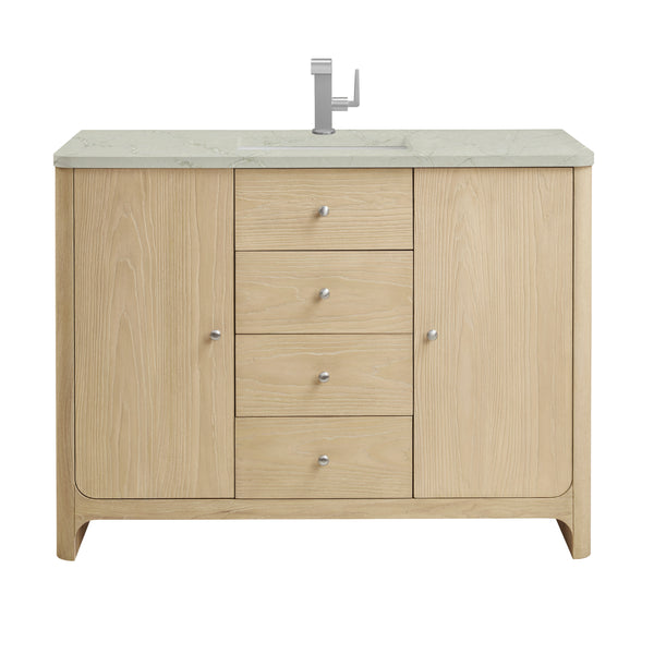 A light wood bathroom vanity with a marble countertop, built-in sink, silver faucet, four central drawers, and two cabinets on either side, each with a round silver knob.