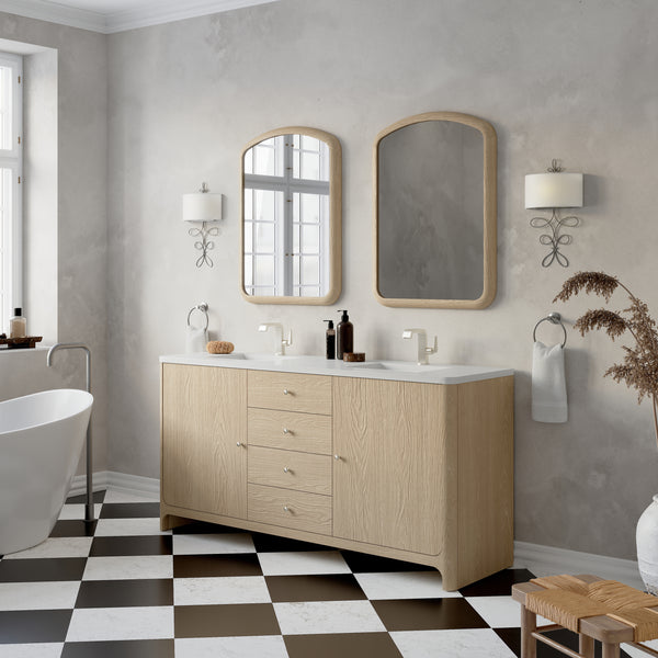 Modern bathroom with a light wood vanity, two rectangular mirrors, wall-mounted lights, a white freestanding bathtub, and a black-and-white checkered tile floor. Dried plants decorate a wooden stool in the corner.