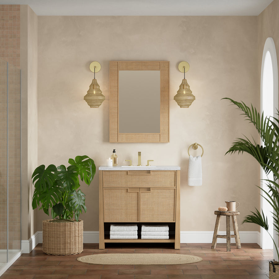 A beige bathroom showcases the Solene 36" Vanity, gold fixtures, a large mirror, two pendant lights, a potted monstera plant, and stacked towels. Sunlight streams through an arched window, highlighting the transitional design.