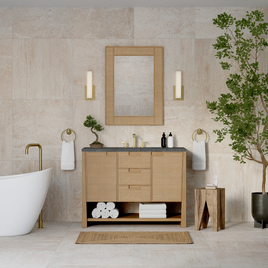 Modern bathroom with beige tile walls, a freestanding white tub with gold fixtures, transitional accents, Solene 48" Vanity in black, round mirror, two sconces, white towels, and a green potted tree on the right.