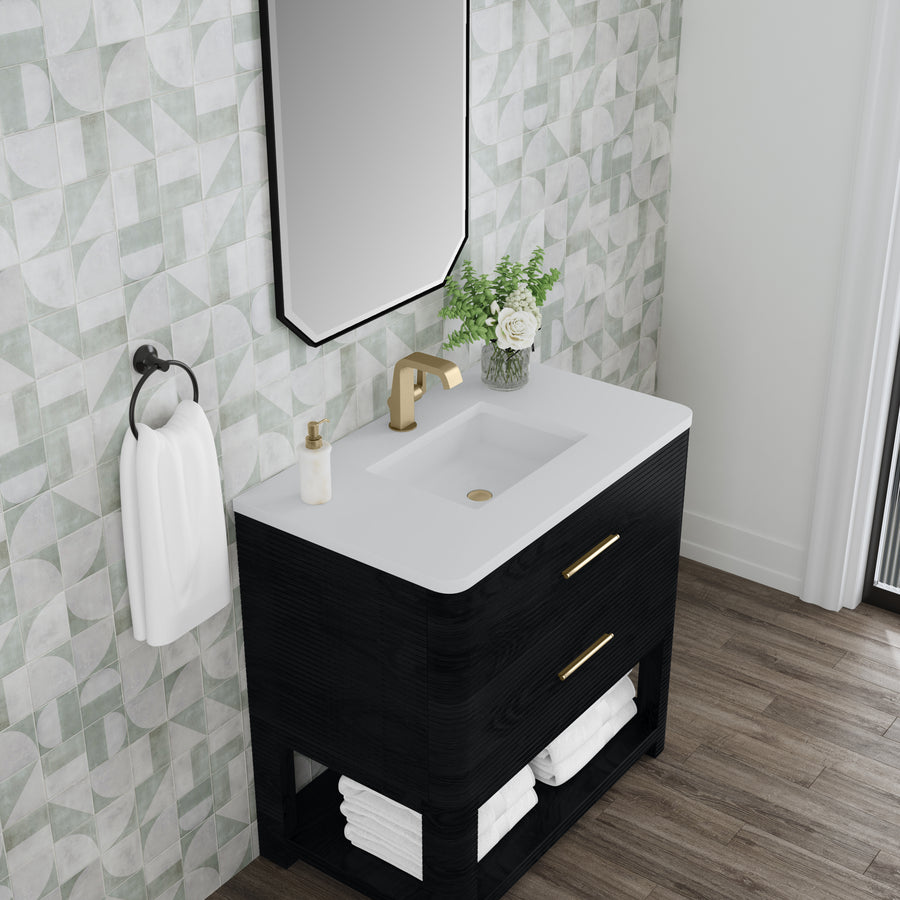A modern bathroom vanity with a white countertop, gold faucet, soap dispenser, and a vase of flowers. The vanity has two drawers with gold handles, white towels below, and a towel ring on a geometric-patterned wall.