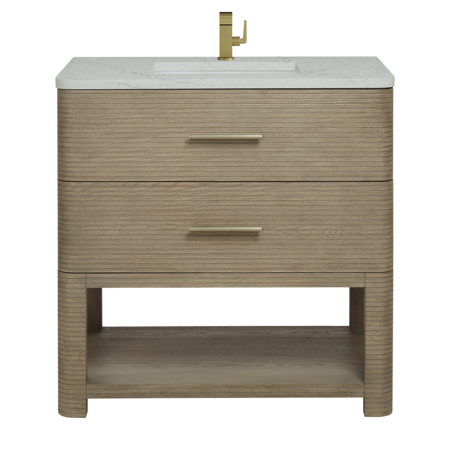 A modern bathroom vanity with a light wood finish, two drawers with gold handles, a white countertop, a built-in sink, and a gold faucet. There is an open shelf at the bottom.