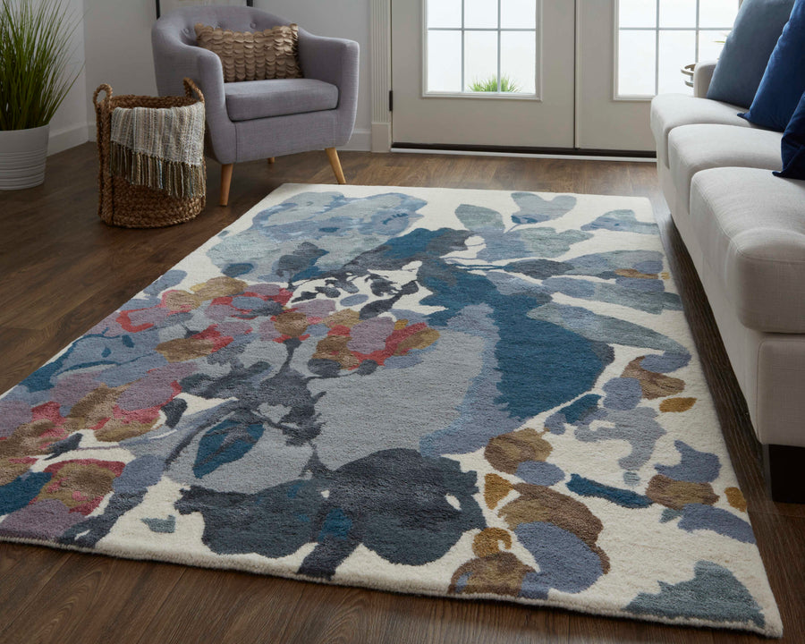 A living room with a floral-patterned area rug in blue, gray, and brown tones on a wooden floor, featuring a gray armchair, a woven basket with a blanket, and a white sofa near glass patio doors.