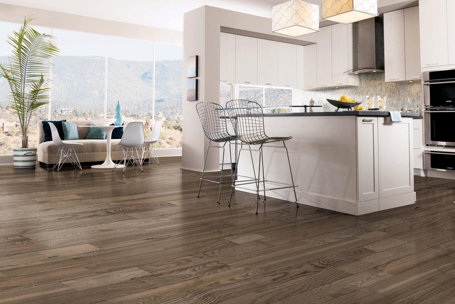 Modern kitchen with white cabinets, a large island with two wire stools, and a dining area by large windows offering mountain views. Dark wood flooring and contemporary decor throughout the open, bright space.