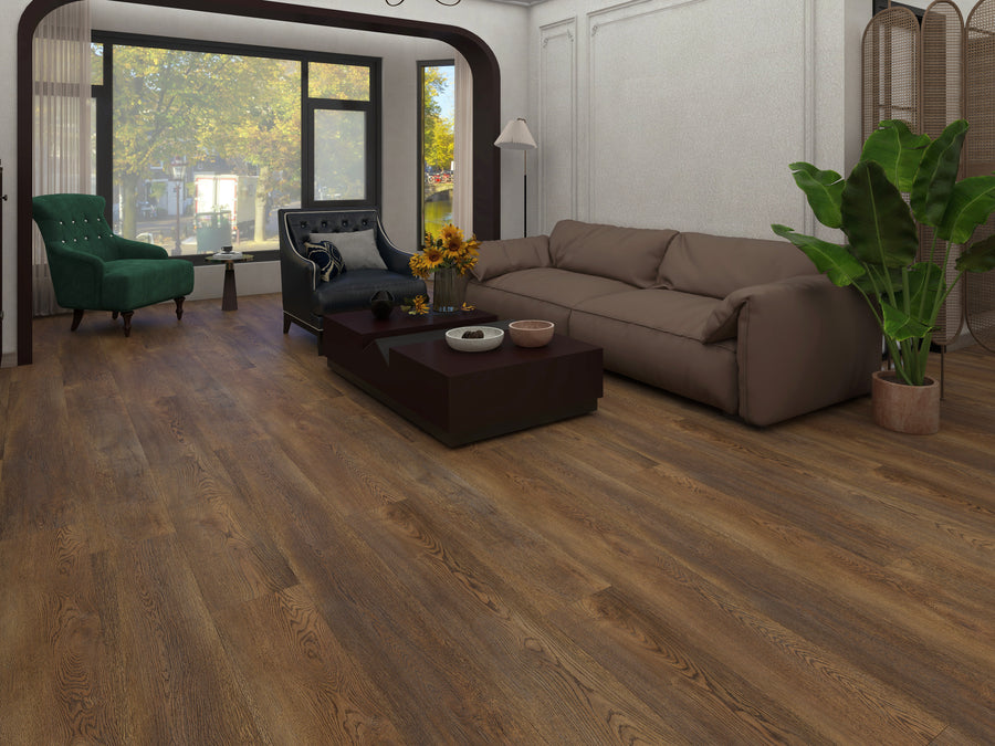 A cozy living room features Hydro Vinyl 7" Waterproof Vinyl Plank flooring with a hardwood look, a brown sofa, dark armchair, green chaise lounge, coffee table, potted plant, floor lamp, and large windows with tree views.
