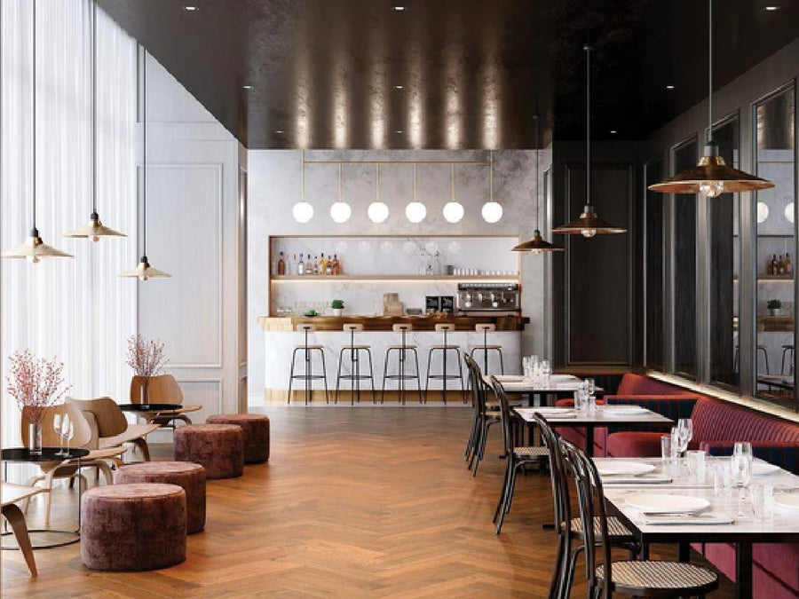 A modern restaurant interior featuring Commercial Hardwood flooring, round ottomans, dining tables, a bar with high stools, pendant lights, and large windows with sheer curtains streaming in natural light.