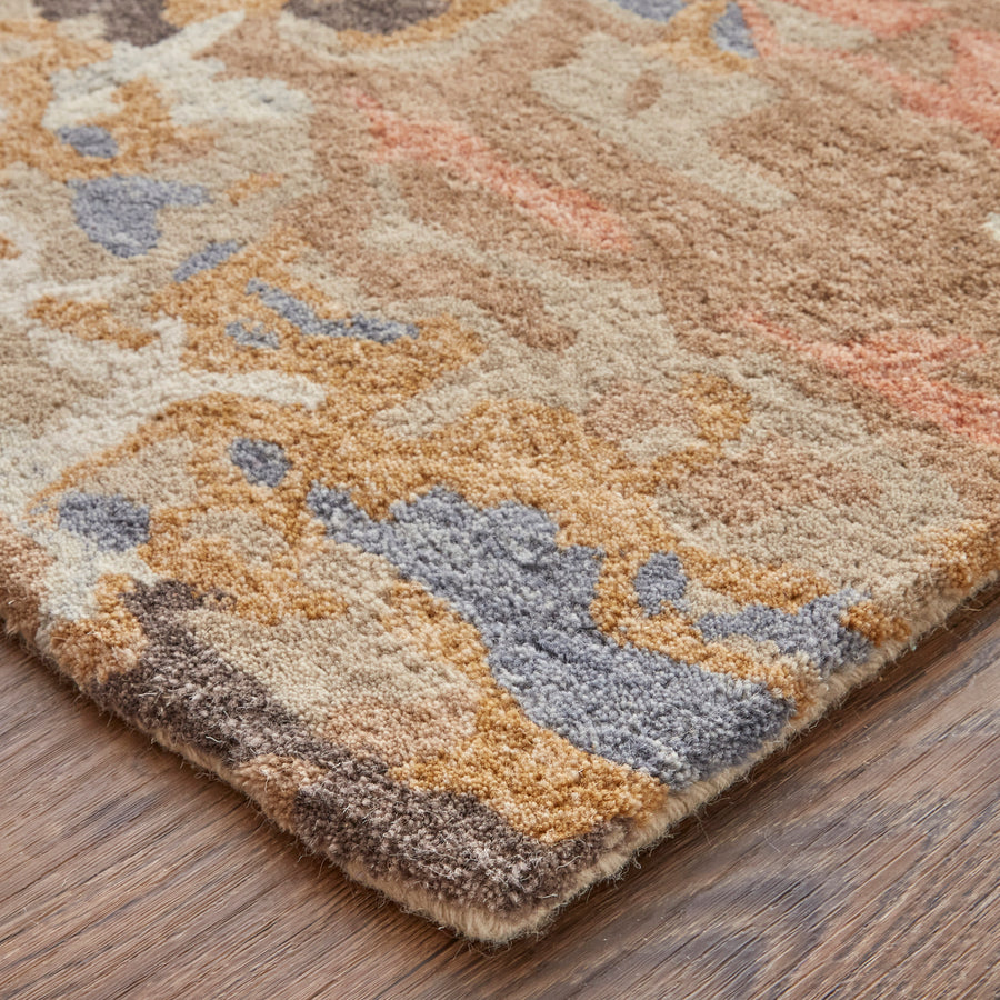 Close-up of the corner of a patterned rug with brown, beige, gray, and orange tones, placed on a wooden floor. The texture of the rug fibers is clearly visible.