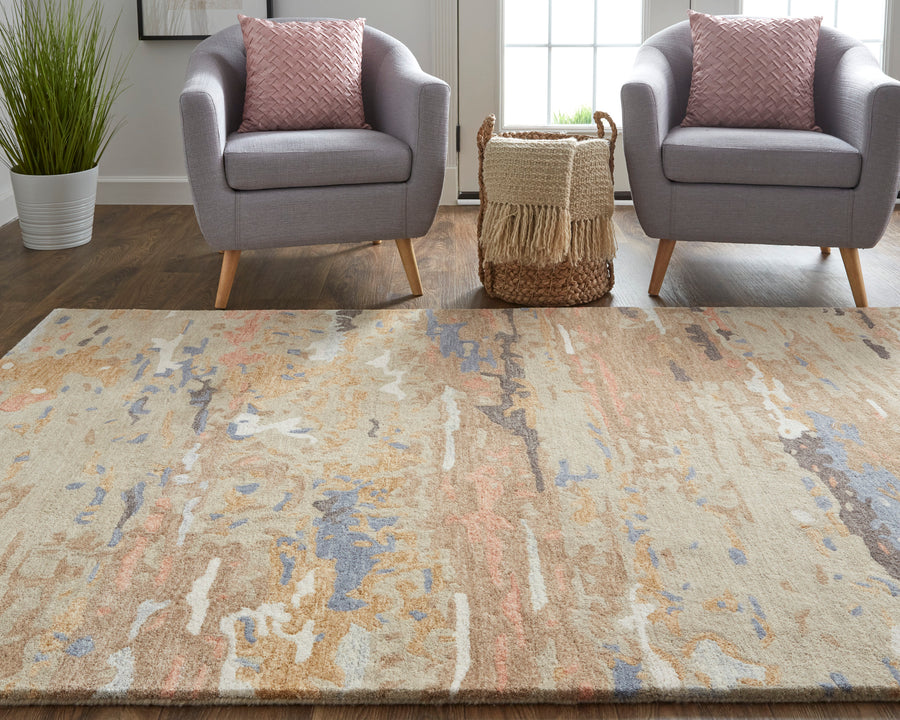 Two gray armchairs with pink patterned pillows face a large, abstract-patterned rug in a living room. A woven basket with a fringe throw sits between the chairs, and a potted plant is in the corner.