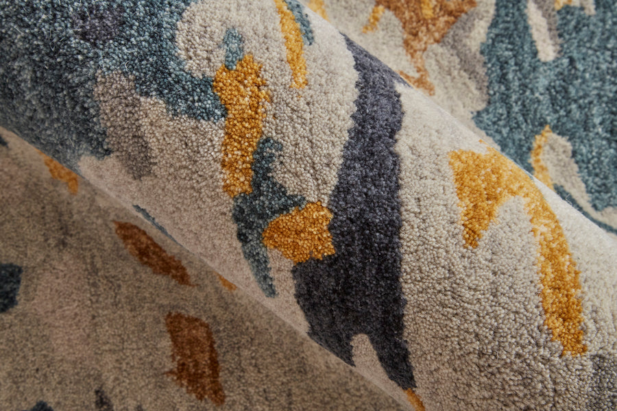 A close-up of a textured carpet with an abstract pattern in shades of blue, gray, gold, and cream. The rug appears soft and plush, with curved and irregular shapes.