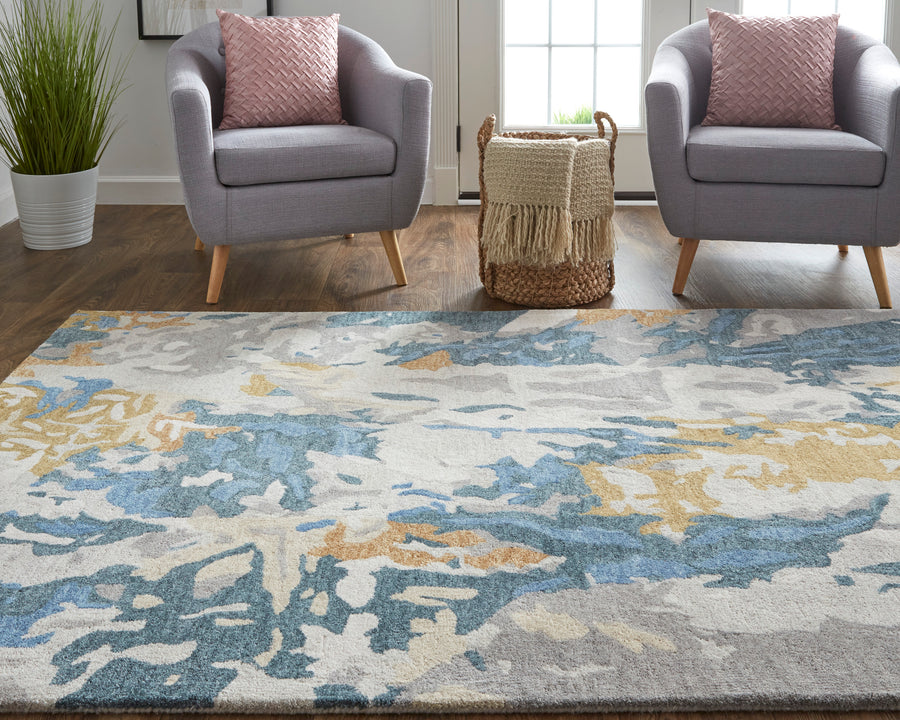 A modern living room with two gray armchairs, pink patterned pillows, a woven basket with a blanket, a tall plant, and a large abstract area rug in blue, gray, and beige tones on a wooden floor.