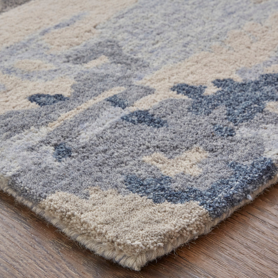 A close-up of a textured rug with a soft, plush surface in shades of beige, gray, and blue, resting on a wooden floor.