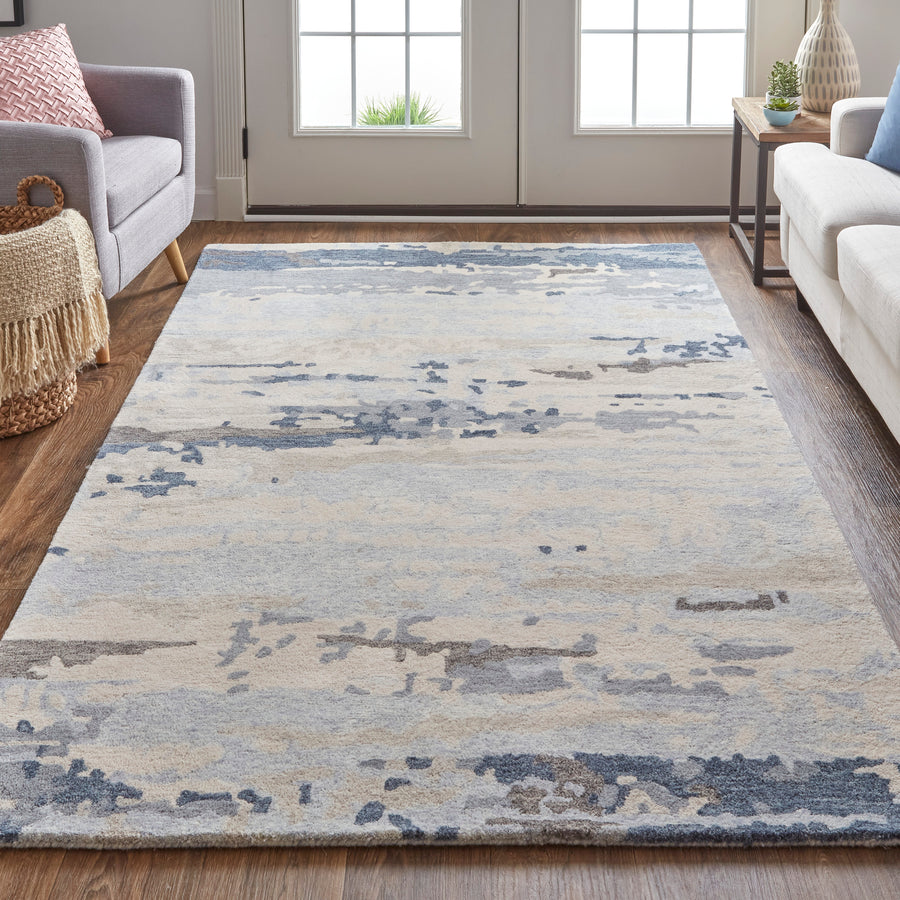 A modern living room with a large, abstract-patterned area rug in shades of blue, gray, and beige on a wooden floor, flanked by a gray sofa on the left and a white sofa on the right.