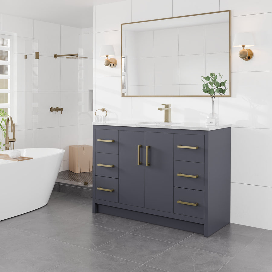 Modern bathroom with a large mirror, wall sconces, a gray vanity with gold handles, white countertop, potted plant, freestanding tub, and glass shower stall in a bright, tiled setting.