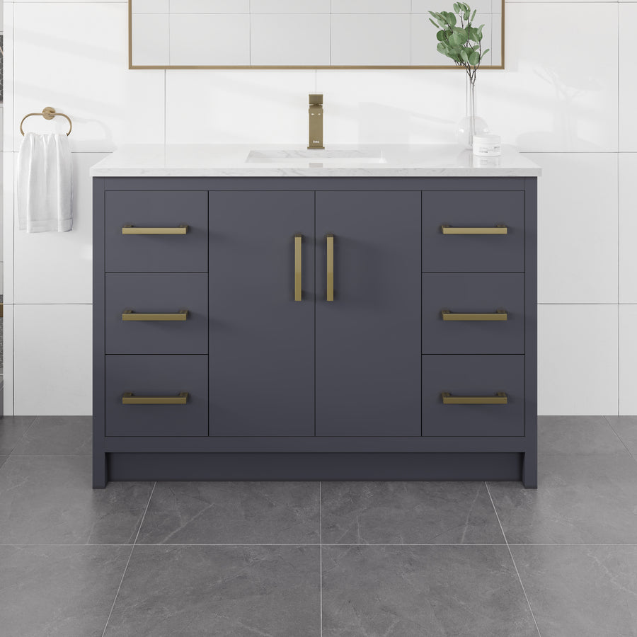 Curio 48″ Vanity in dark blue features gold handles and a sleek Carrara quartz top. This 48″ vanity includes a single sink, a towel hanging on the left side, and is complemented by a green plant and mirror above it on a tiled wall, with gray tiles covering the floor.